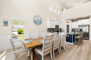 A spacious kitchen with white cabinetry, a large wall clock, and a dining area with wooden tables and chairs.