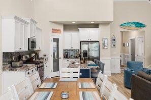 A modern kitchen with white cabinetry, a stainless steel refrigerator, and a dining area with a wooden table and chairs.