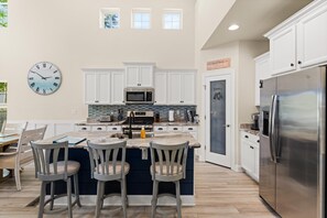 A kitchen with white cabinets, a stainless steel refrigerator, a clock, and a bar area with stools.