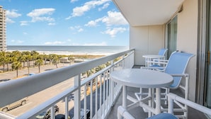 A balcony with a view of the beach and ocean, featuring white chairs and a small table. - Ocean View 2 bedroom, 2 bath unit in South Hampton Tower. (Myrtle Beach)