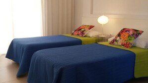 Una habitació amb dos llits, cadascun amb un llençol blau i un coixí de colors. Hi ha una tauleta de nit amb una làmpada entre els llits.