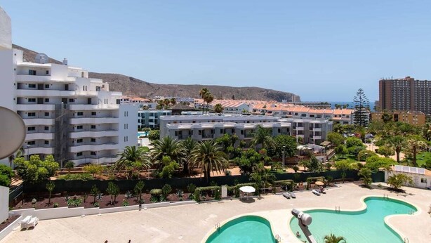 Un complex turístic amb diverses piscines, un paisatge de muntanyes i un cel serè.