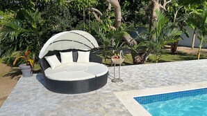 A round outdoor seating area with a canopy, a pool, and tropical plants.
