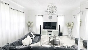 A modern living room with a black leather sofa, a glass coffee table, a flat-screen TV, and decorative vases.