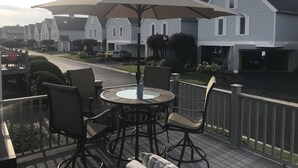 A patio with a round table and chairs, an umbrella, and a view of white houses in the background. - Waterfront home;heated pool & spa: walk to public beach; food, bars, live music! (Port Clinton)