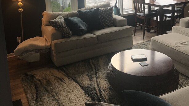 A living room with a sofa, a coffee table, and a lamp. There are large windows with a view of the outside. - Waterfront home;heated pool & spa: walk to public beach; food, bars, live music! (Port Clinton)