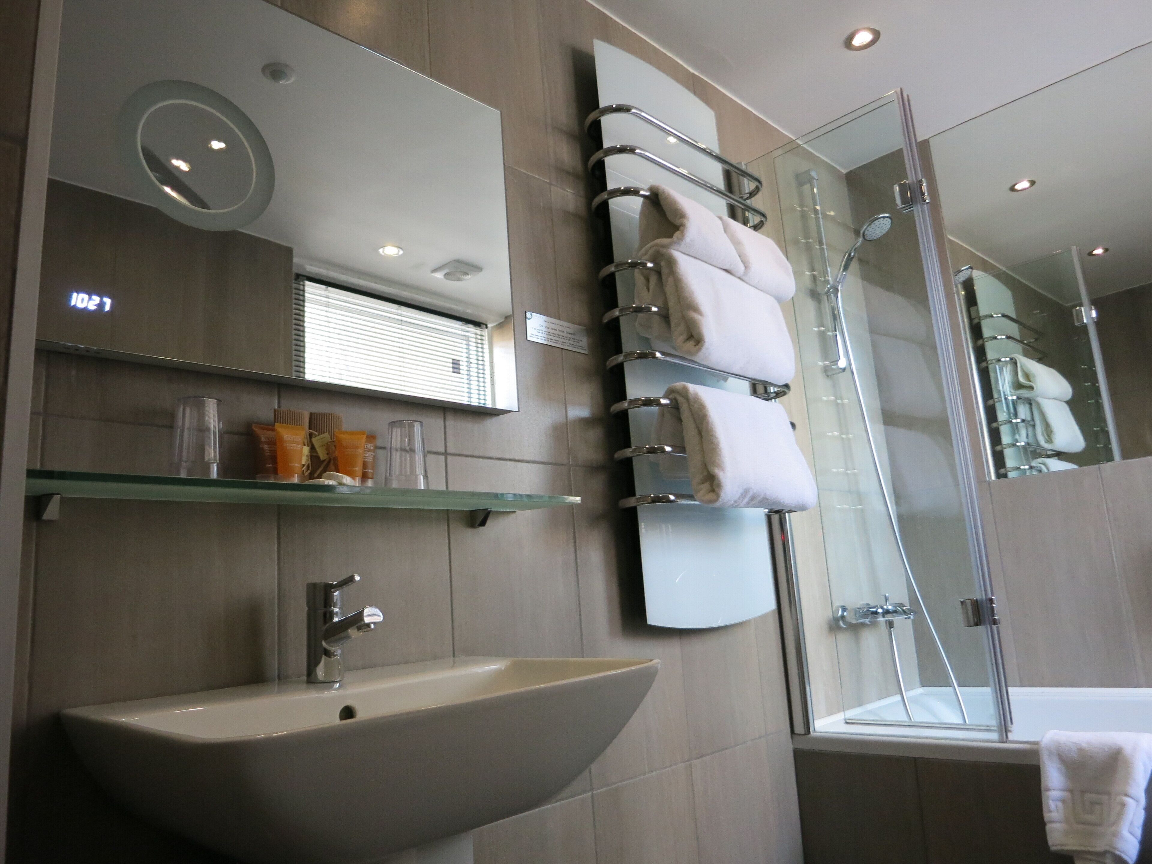 Un baño moderno con un lavamanos grande, una cabina de ducha de vidrio y un espejo con toallero.