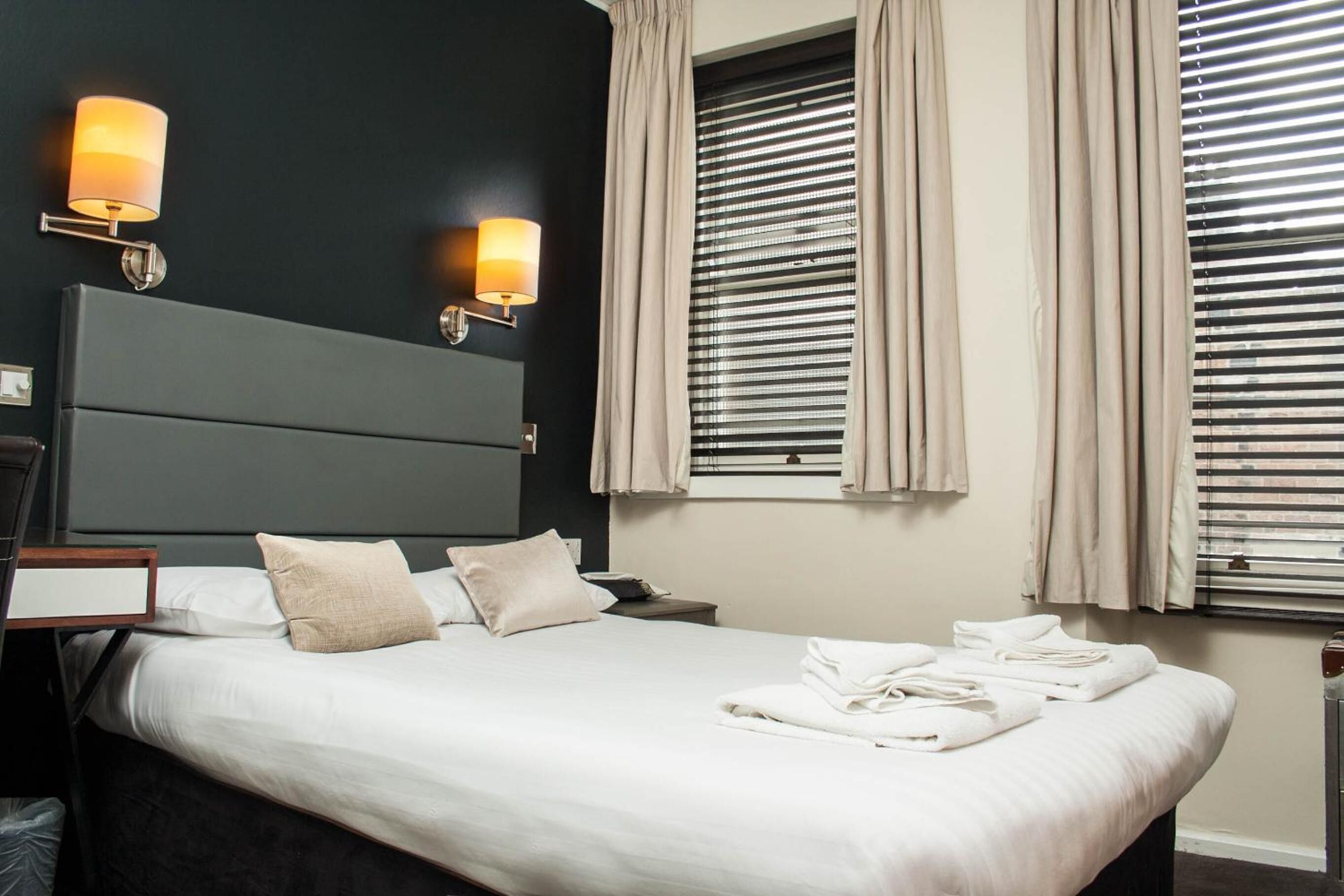 A neatly made bed with white linens, a bedside table with a lamp, and a headboard.