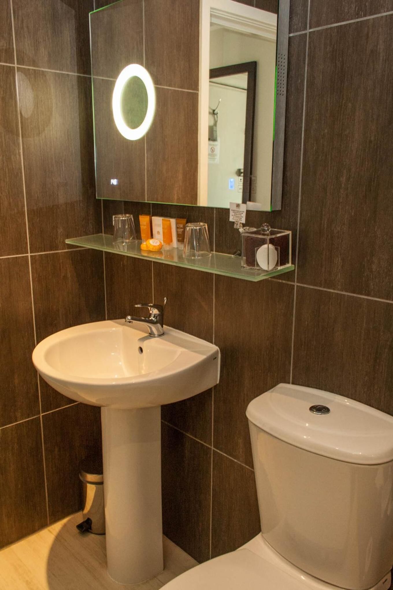 Ein Badezimmer mit einem weißen Waschbecken, einer Toilette und einem Glasregal darüber.