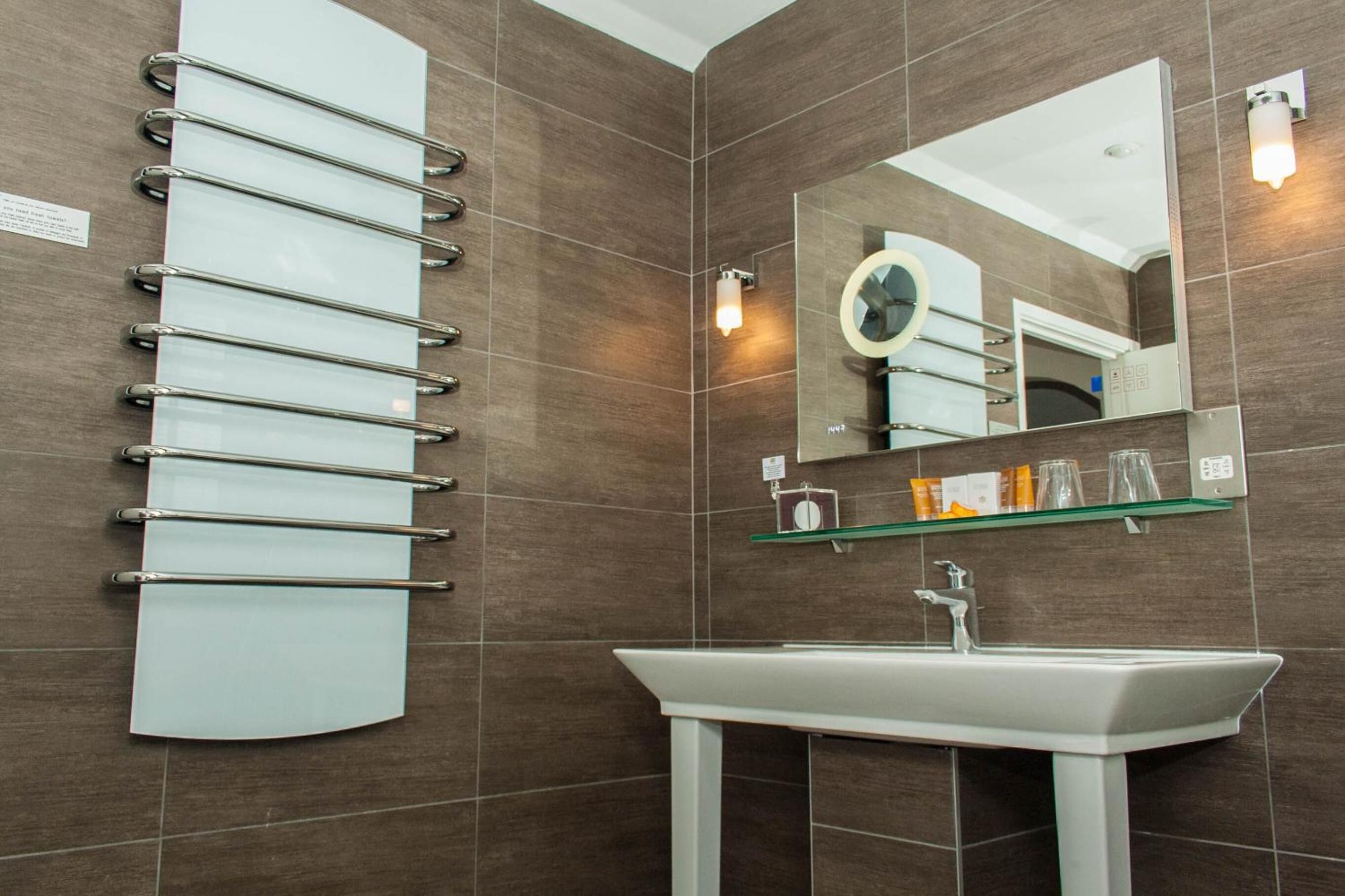 A modern bathroom with a large mirror, a white sink, and a glass shelf with toiletries.