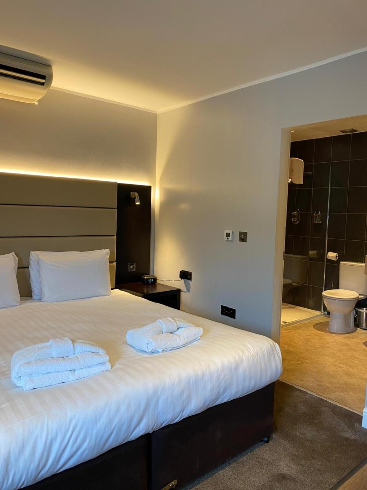 Camera d'albergo con un letto grande, comodini, un climatizzatore e bagno con toilette e doccia.