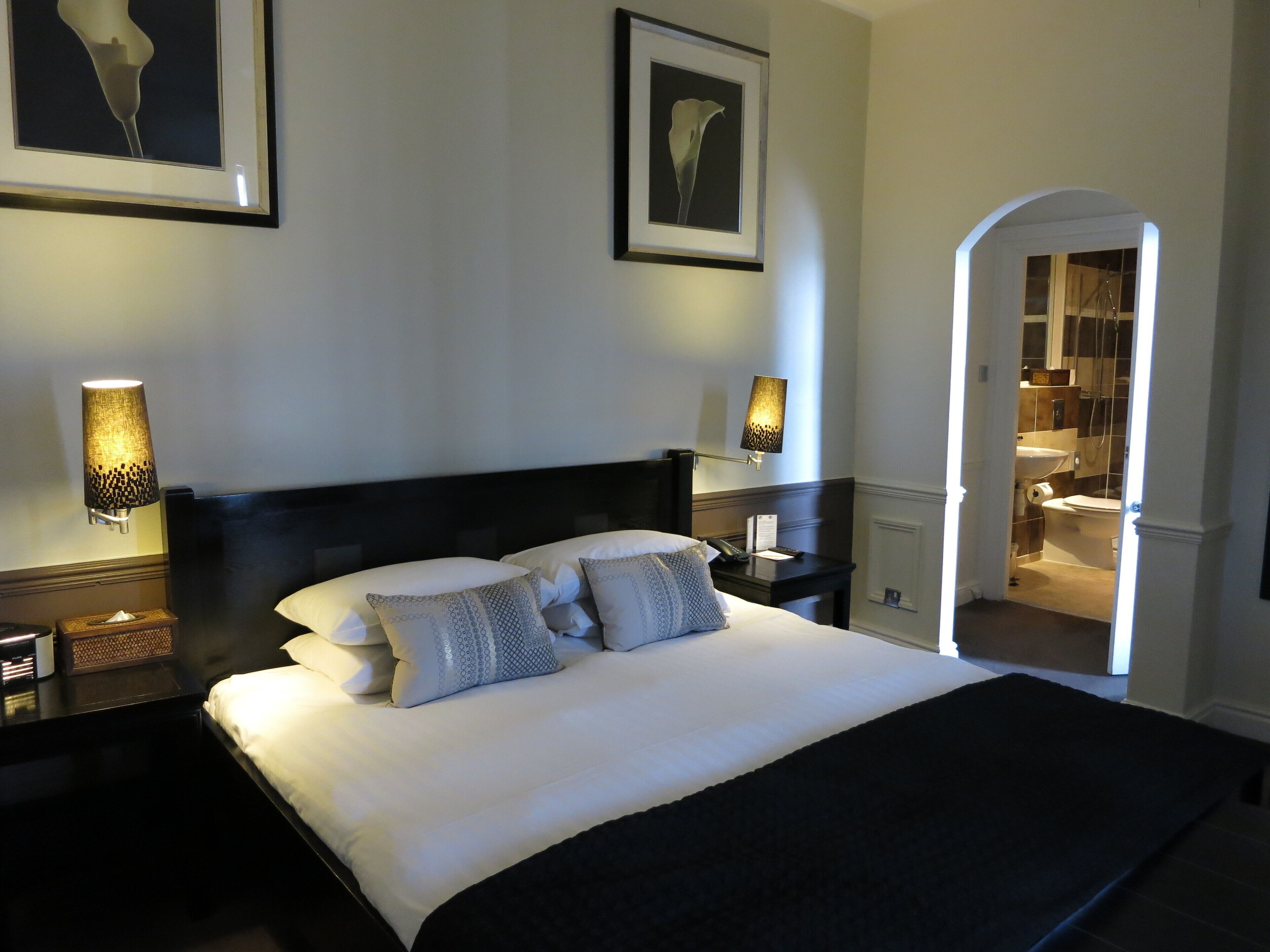 A hotel room with a large bed, two bedside tables with lamps, a nightstand, and a framed picture on the wall.