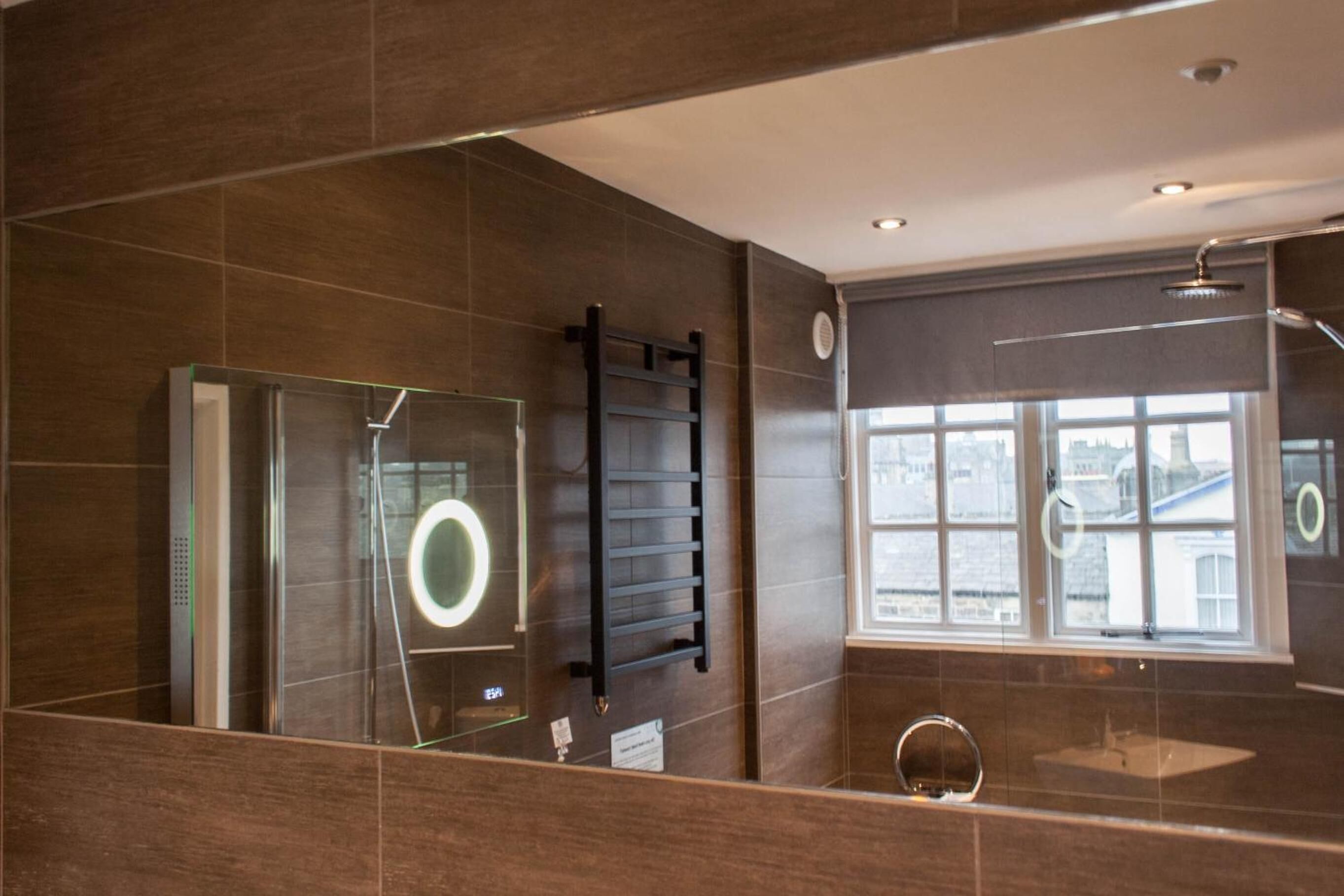 A modern bathroom with a glass shower enclosure, a towel rack, a sink with a mirror, and a window with a view of buildings.