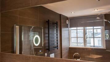 A modern bathroom with a glass shower enclosure, a towel rack, a sink with a mirror, and a window with a view of buildings.