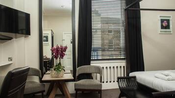 Ein Hotelzimmer mit Bett, Schreibtisch mit Stuhl, Fernseher, Fenster mit Jalousien und Heizkörper.