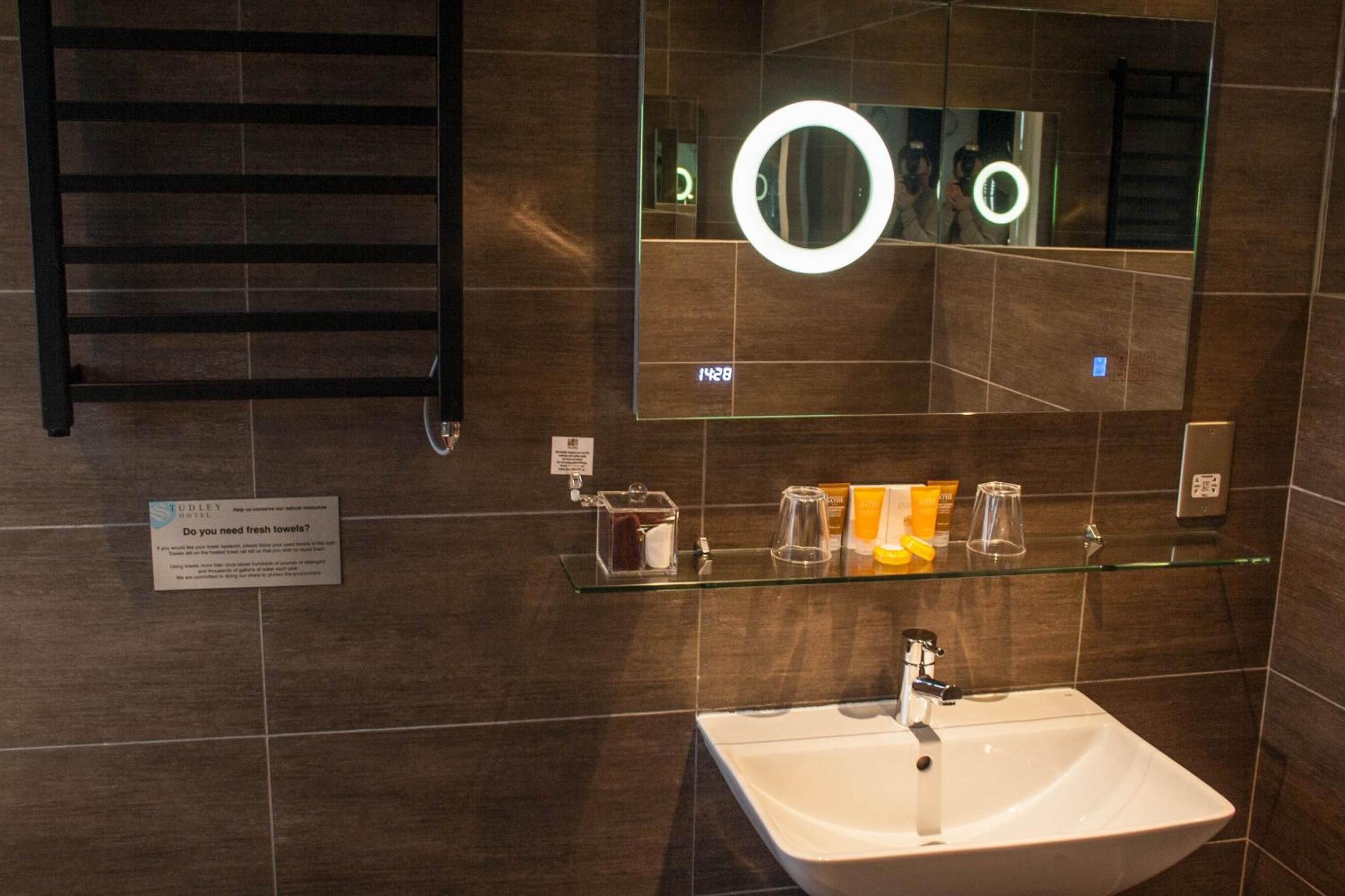 A modern bathroom with a large mirror, a glass shelf with toiletries, and a towel rack.