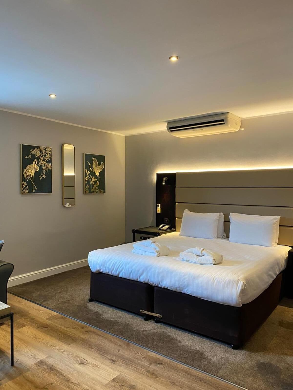 A modern hotel room with a large bed, bedside tables, an air conditioning unit, and artwork on the walls.