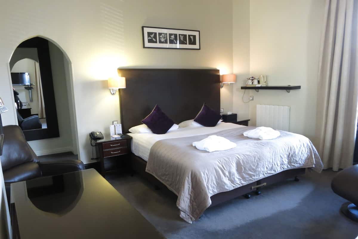 A hotel room with a large bed, a nightstand, a desk, a chair, and a mirror.