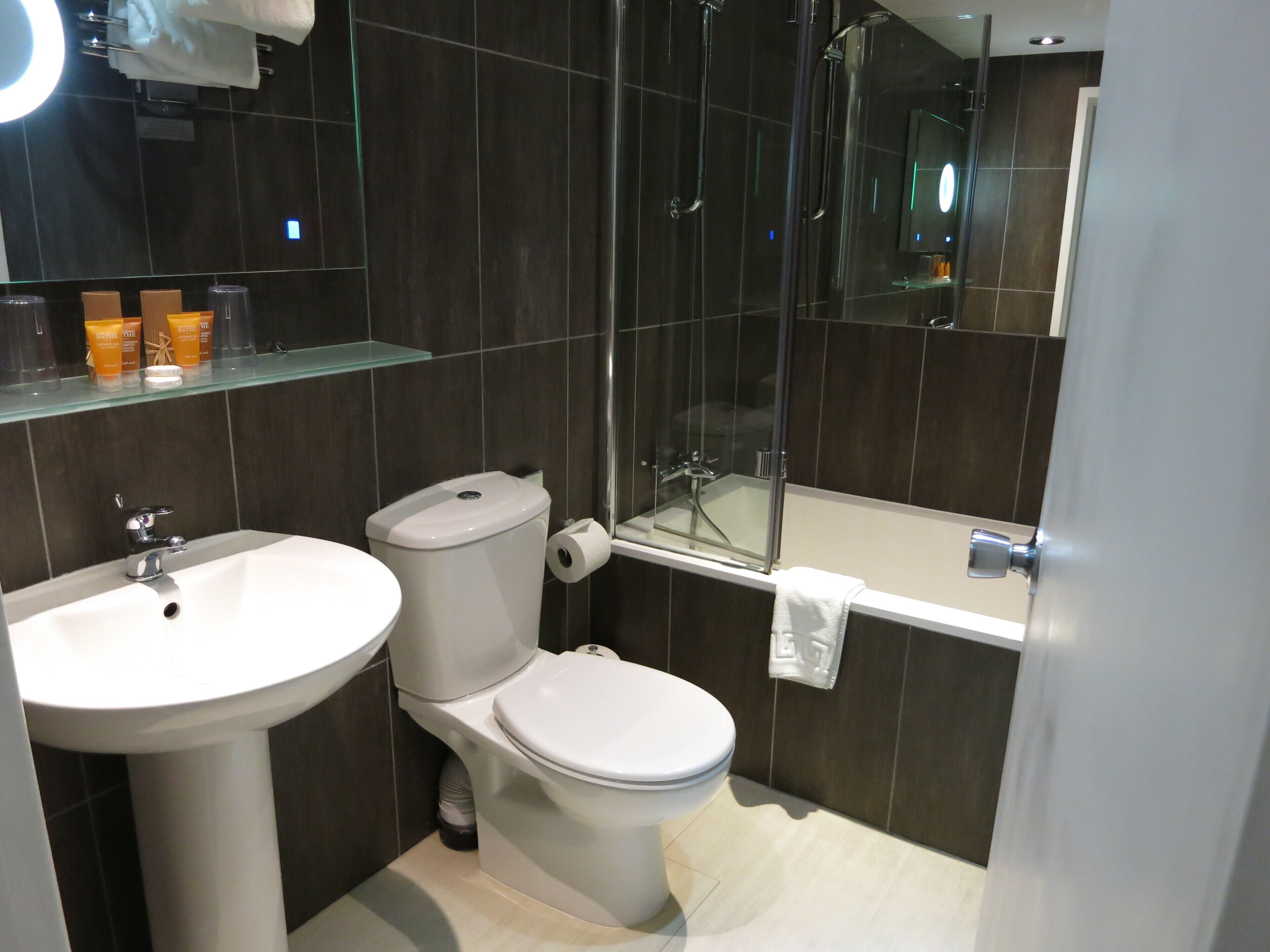 A modern bathroom with a white sink, toilet, and bathtub. There is a glass shower enclosure and a mirror above the sink.