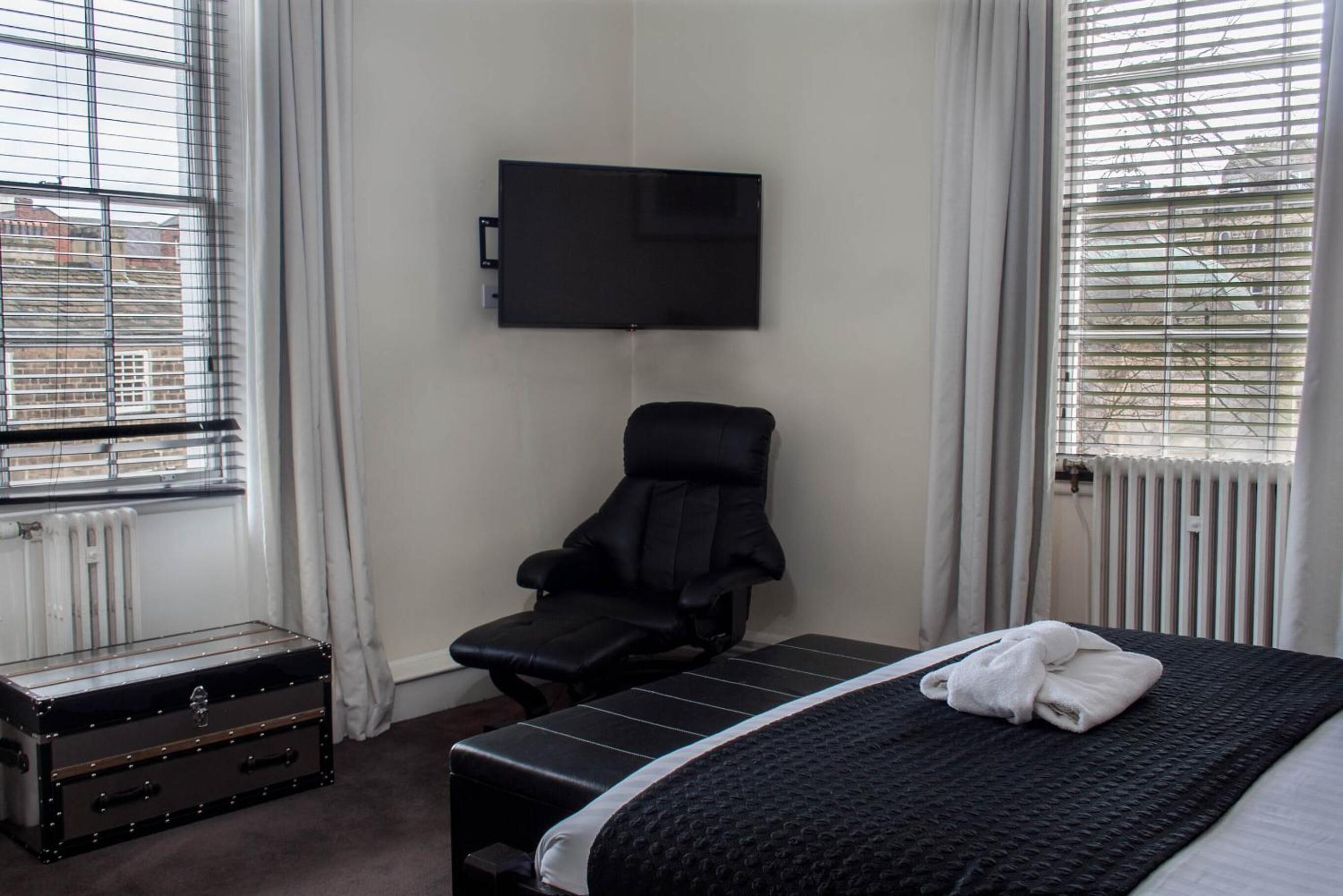 Una habitación de hotel con una cama, una silla, un televisor y una maleta.