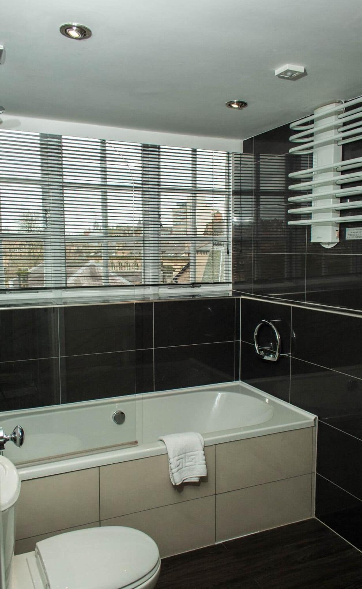 Un baño moderno con bañera, inodoro y ventana con persianas.