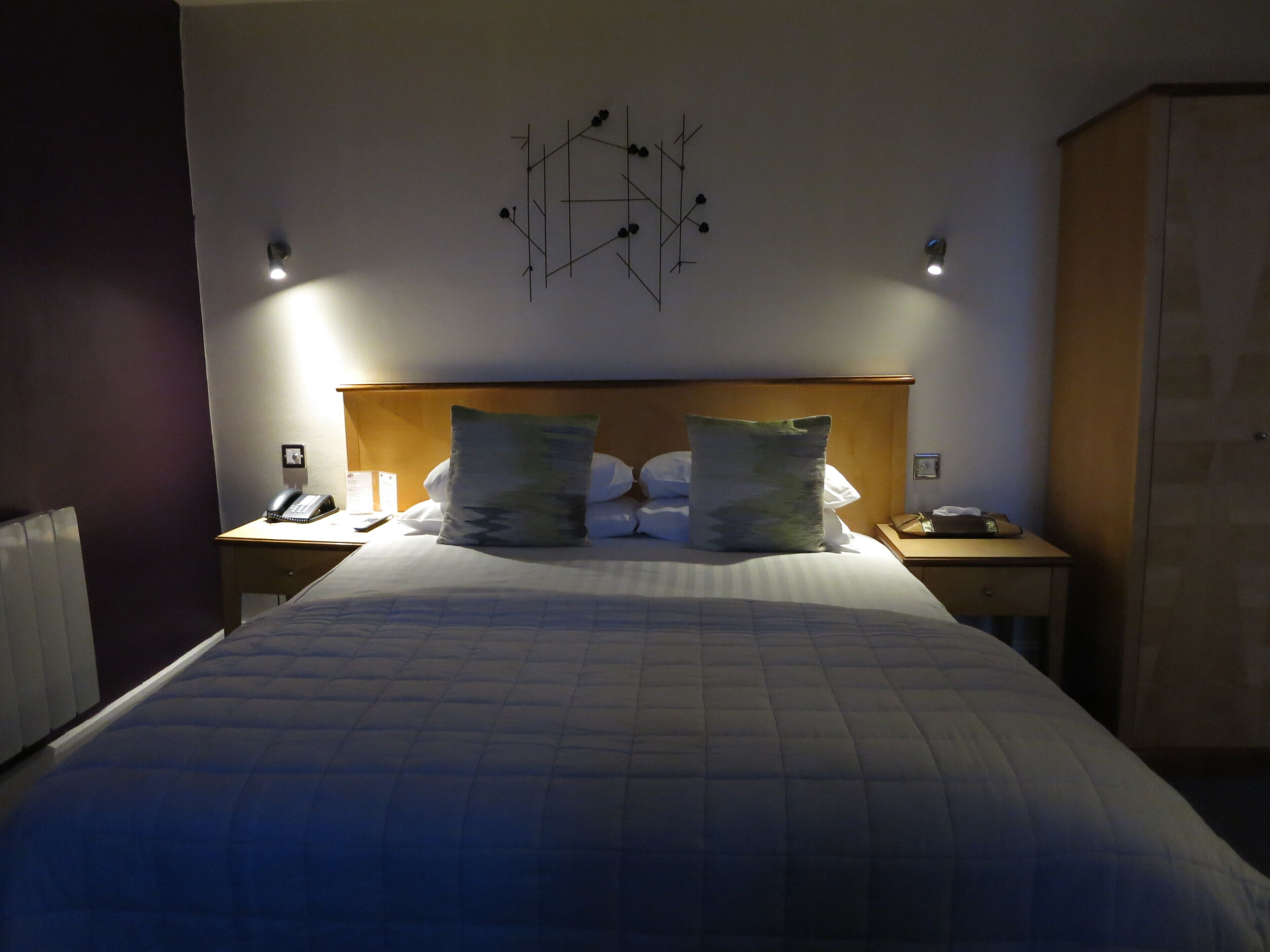 Habitación de hotel con una cama grande, dos mesitas de noche, cabecera de madera y una obra de arte abstracta colgada en la pared.
