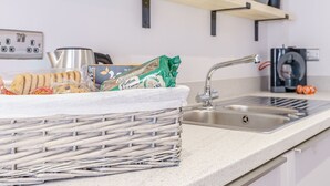 Una cocina con una cesta de mimbre que contiene galletas y bolsitas de té, un lavamanos de acero inoxidable y una cafetera.