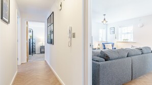 Un salón moderno con un sofá seccional gris, suelo de madera en espiga y un pasillo que conduce a un baño.