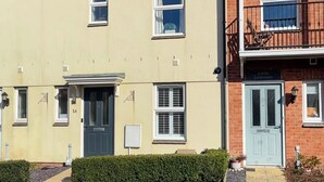 A two-story residential building with a beige facade, numbered doors, and a balcony with a metal railing. - 4 bedroom accommodation in Sidmouth (Sidmouth)