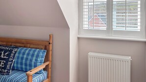 A room with a sloped ceiling, a wooden bench with blue and white striped cushions, and a white radiator. - 4 bedroom accommodation in Sidmouth (Sidmouth)