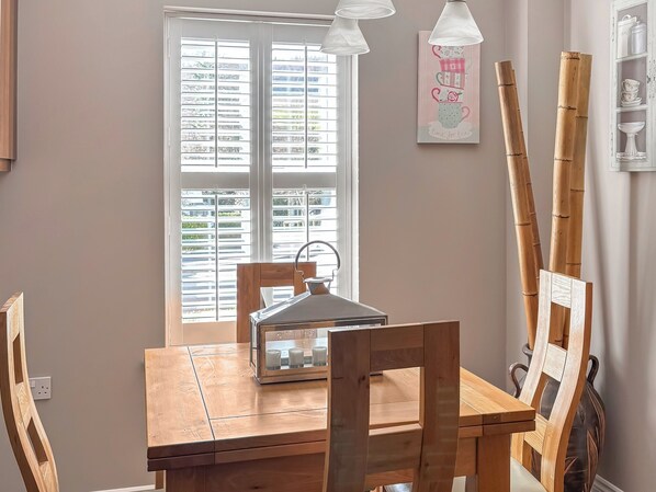 A dining area with a wooden table and chairs, a window with blinds, and a wall-mounted light fixture.