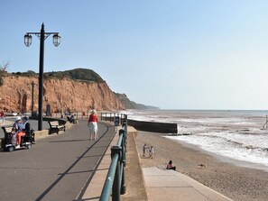 A coastal promenade with benches, a paved walkway, and a cliffside.