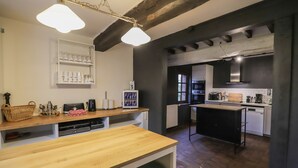 Una cocina con encimeras de madera, una isla central y un horno empotrado. Hay un armario blanco con cristalería y un colgante de luz.