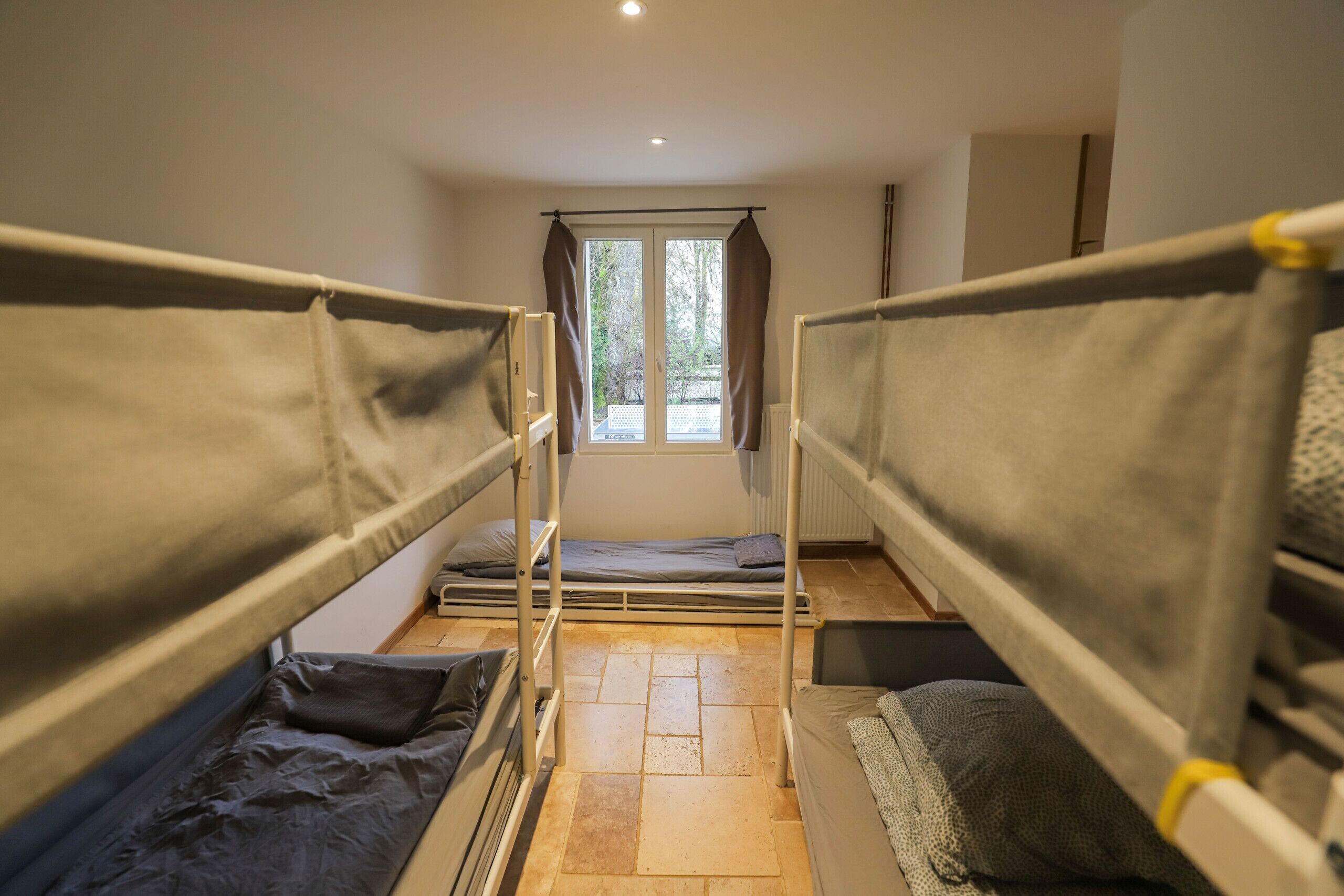 Une chambre de dortoir avec des lits superposés, une fenêtre avec des rideaux et un radiateur.