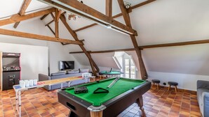 Een ruime kamer met een pooltafel, een bank, een televisie en een pingpongtafel.
