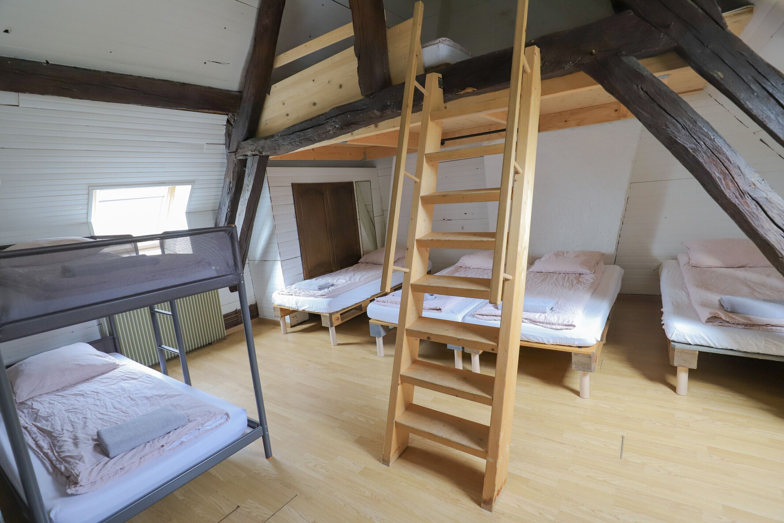 Une chambre de dortoir avec des lits superposés, une échelle en bois et une fenêtre.