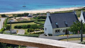 Panorama costiero con una casa, una spiaggia e una barca a vela.
