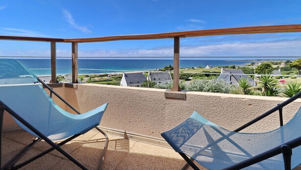 Un balcone con due sedie blu e un tavolo, con vista su una spiaggia e l'oceano.