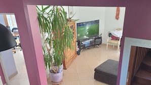 Un salon avec un téléviseur, un pouf rouge, un meuble en bois et une plante en pot.