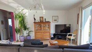 Un salon moderne avec un grand canapé, un meuble en bois, un téléviseur et un coin repas avec des chaises.