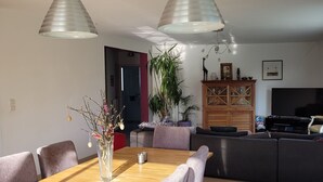 Un espace repas moderne avec une table et des chaises en bois, deux lampes suspendues et une plante en pot.