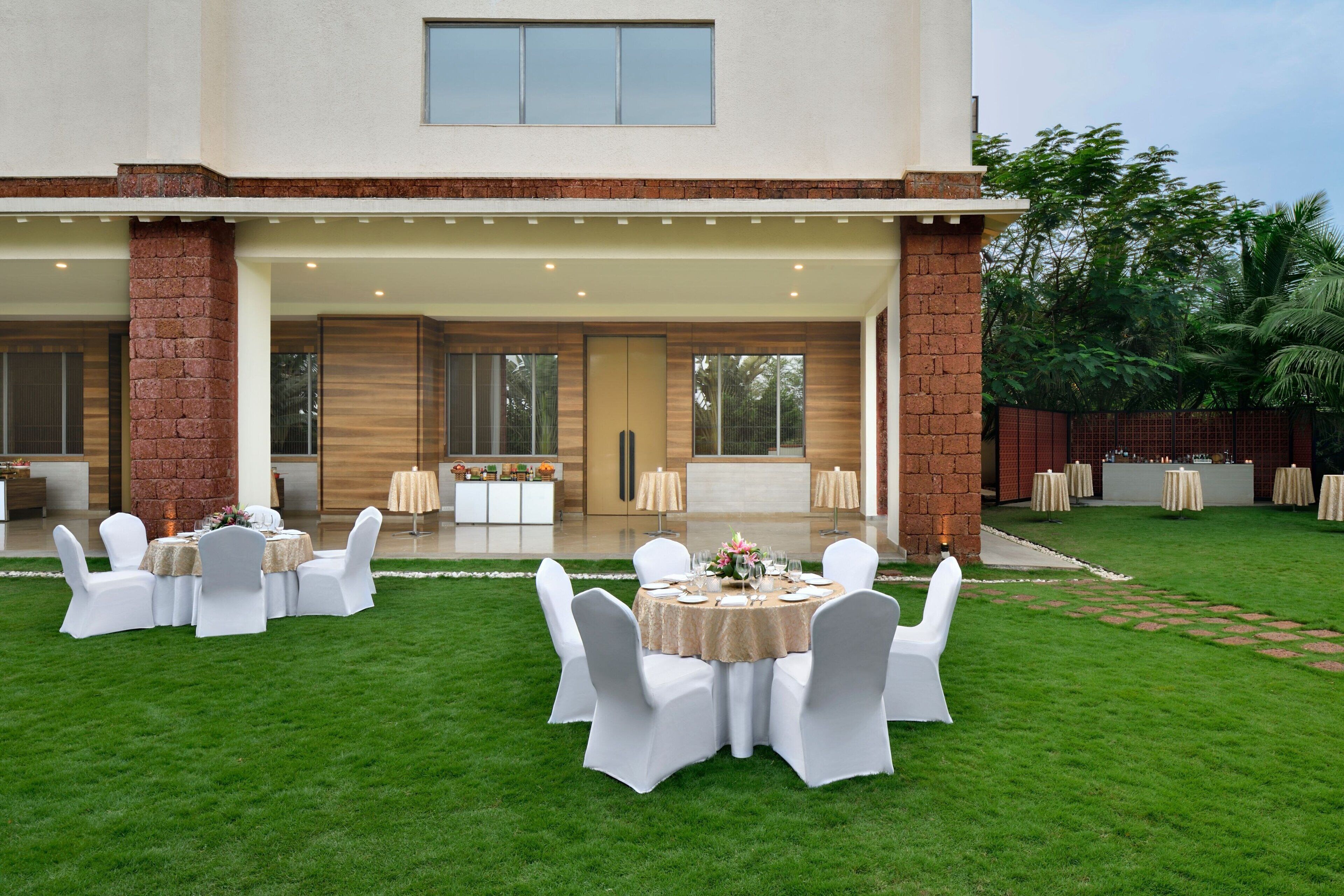 Une vaste terrasse extérieure dotée de plusieurs tables rondes et de chaises blanches, entourée d’une pelouse bien entretenue.