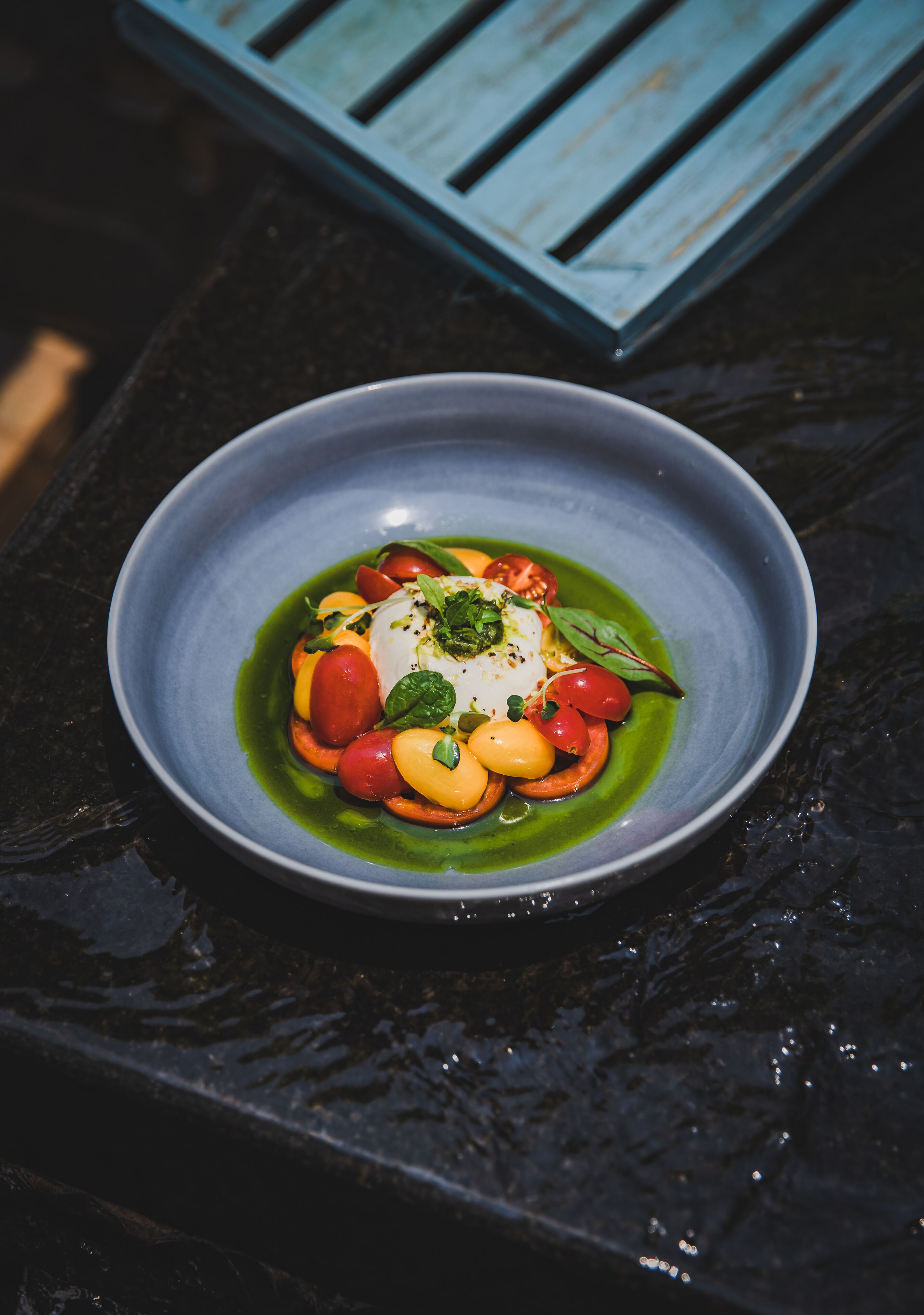 A bowl of food with a white center, surrounded by tomatoes and green sauce, on a dark surface.