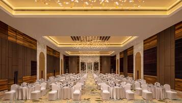 A banquet hall with round tables and white chairs, a chandelier, and a patterned carpet.