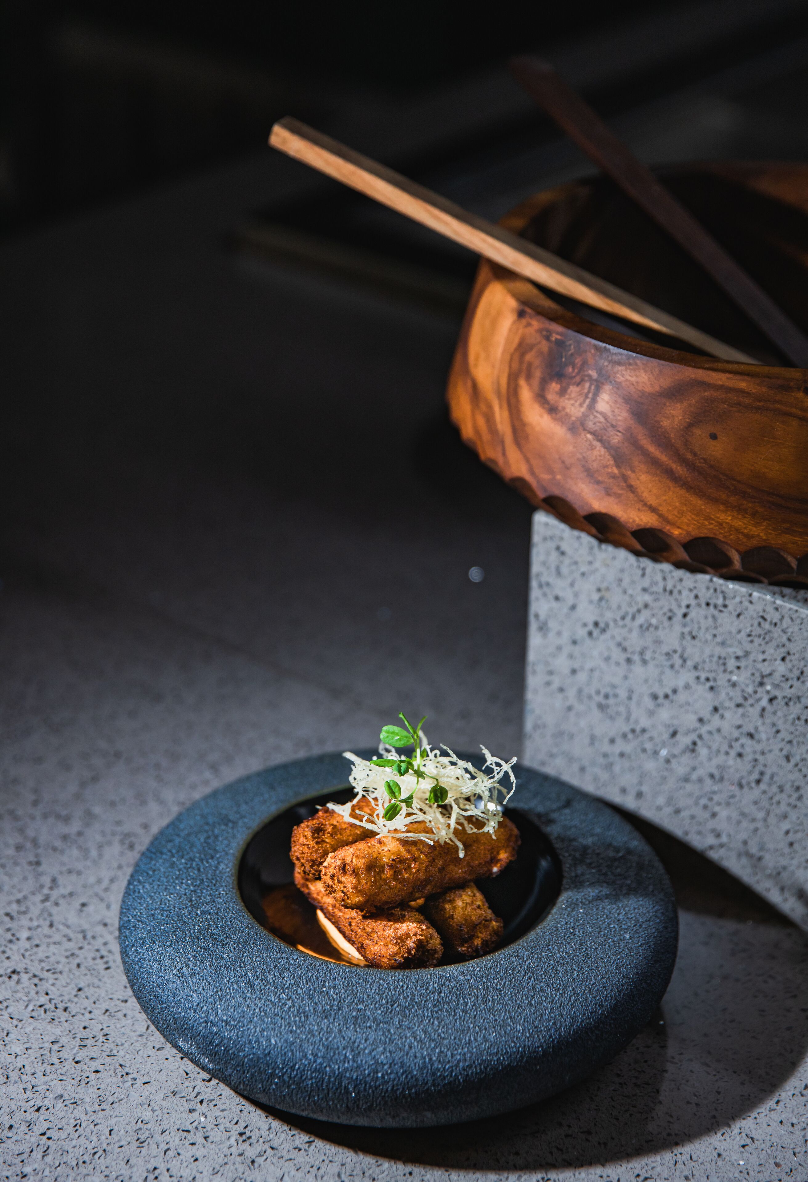 Un plato cerámico azul oscuro y redondo con un alimento y decoración, sobre una superficie moteada.