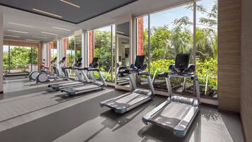 Un gimnasio moderno con cintas de correr, amplias ventanas y vistas al exterior a zonas verdes.
