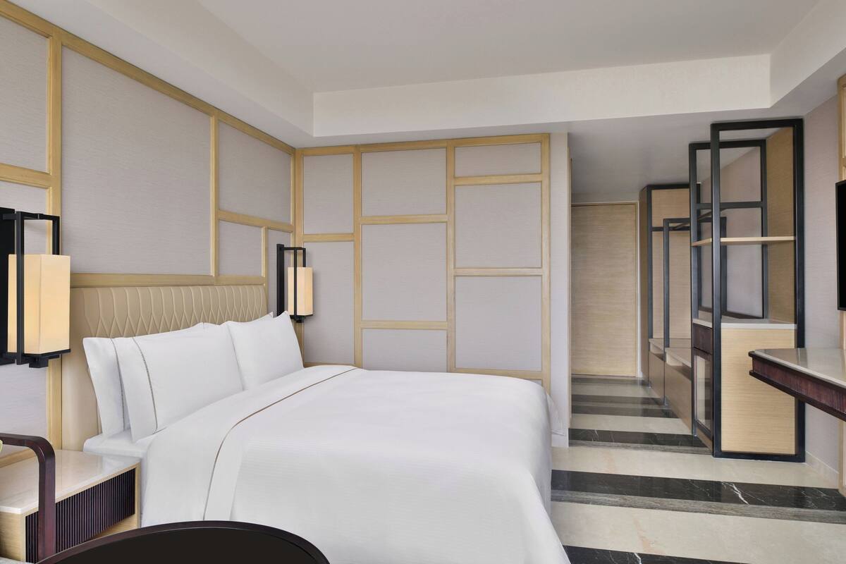 A hotel room with a large bed, a desk, and a mirror.