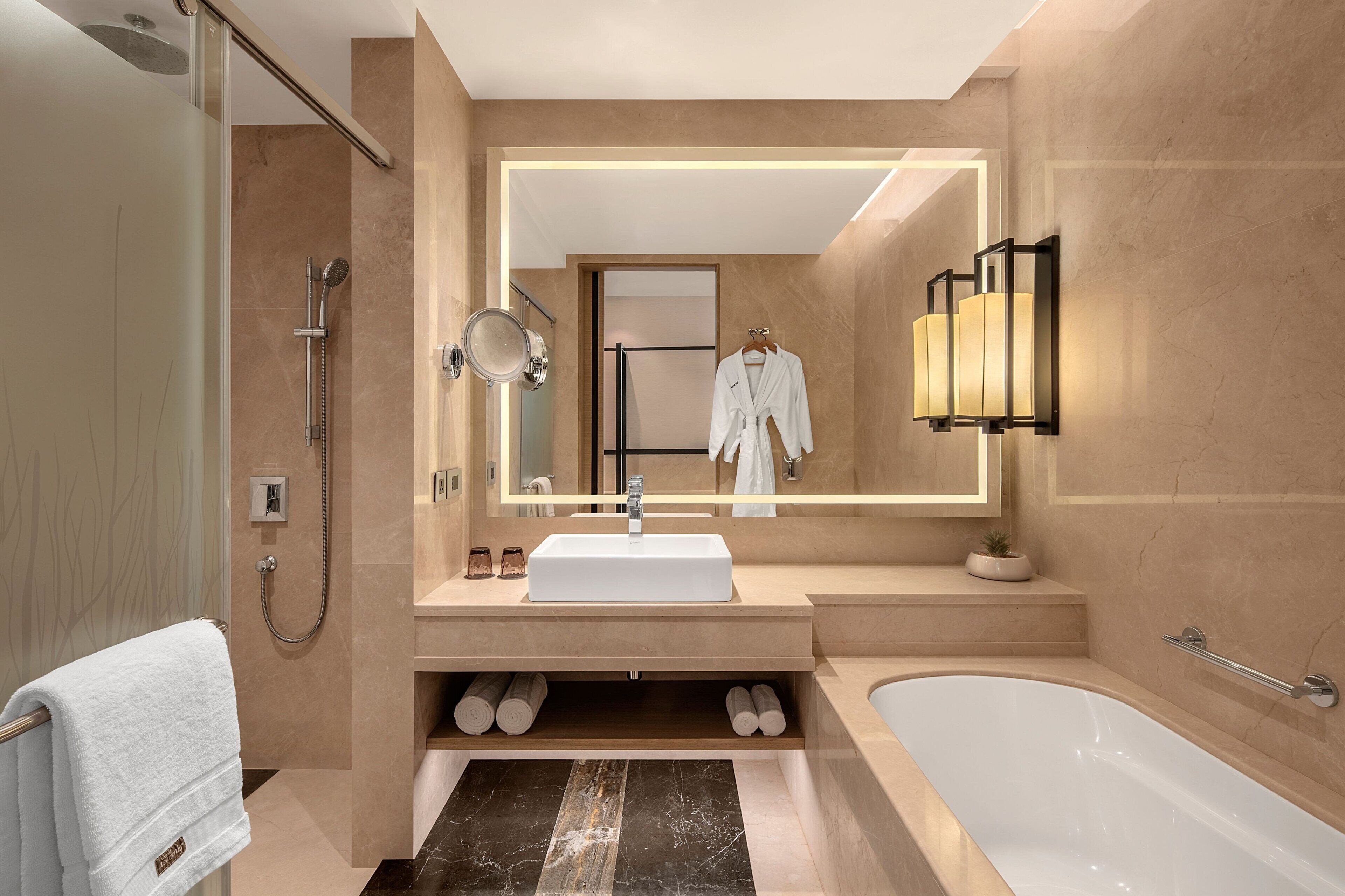 A modern bathroom with a large mirror, a white sink, a bathtub, and a shower.