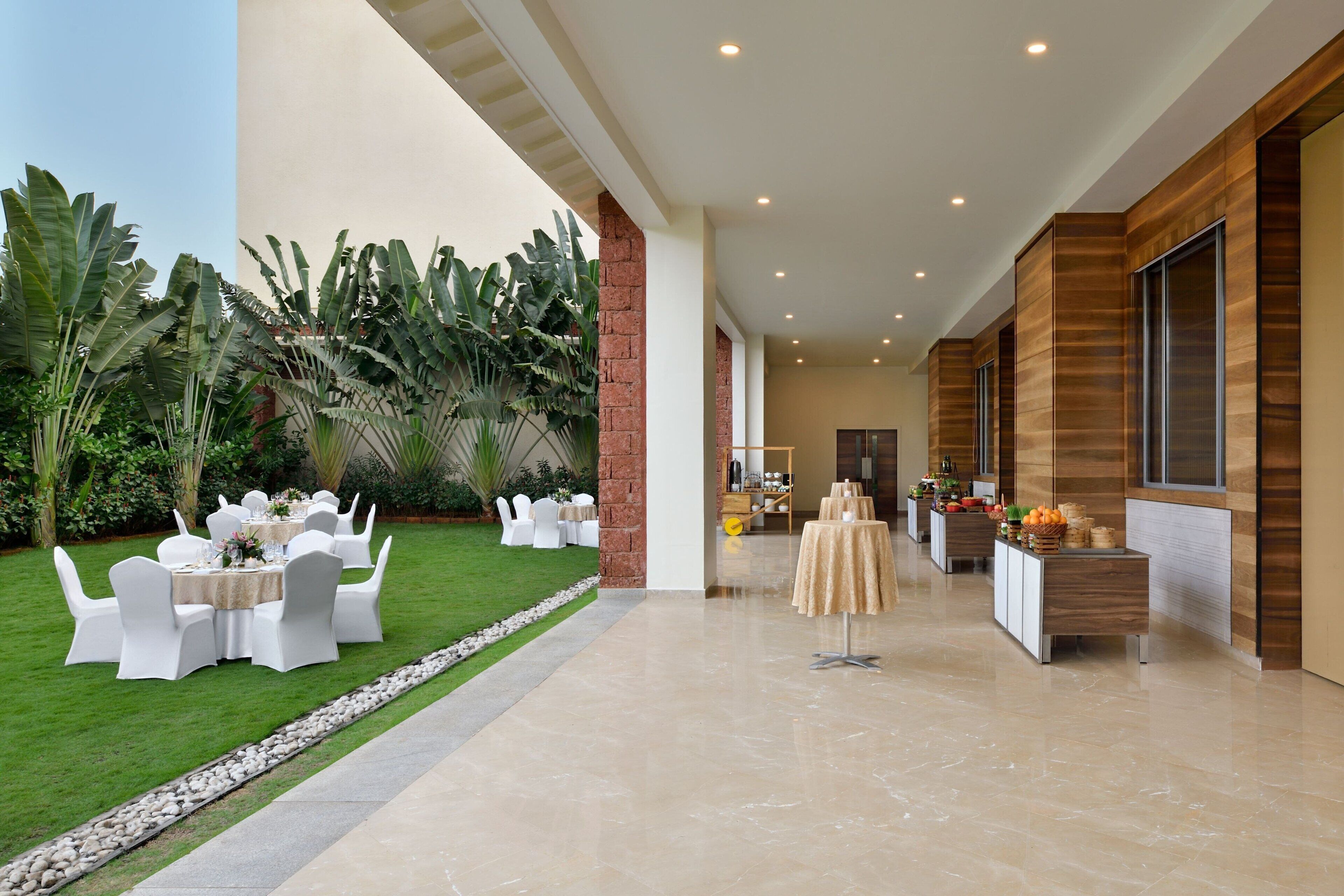 A well-maintained outdoor dining area with white tables and chairs, surrounded by lush greenery and a clear pathway.