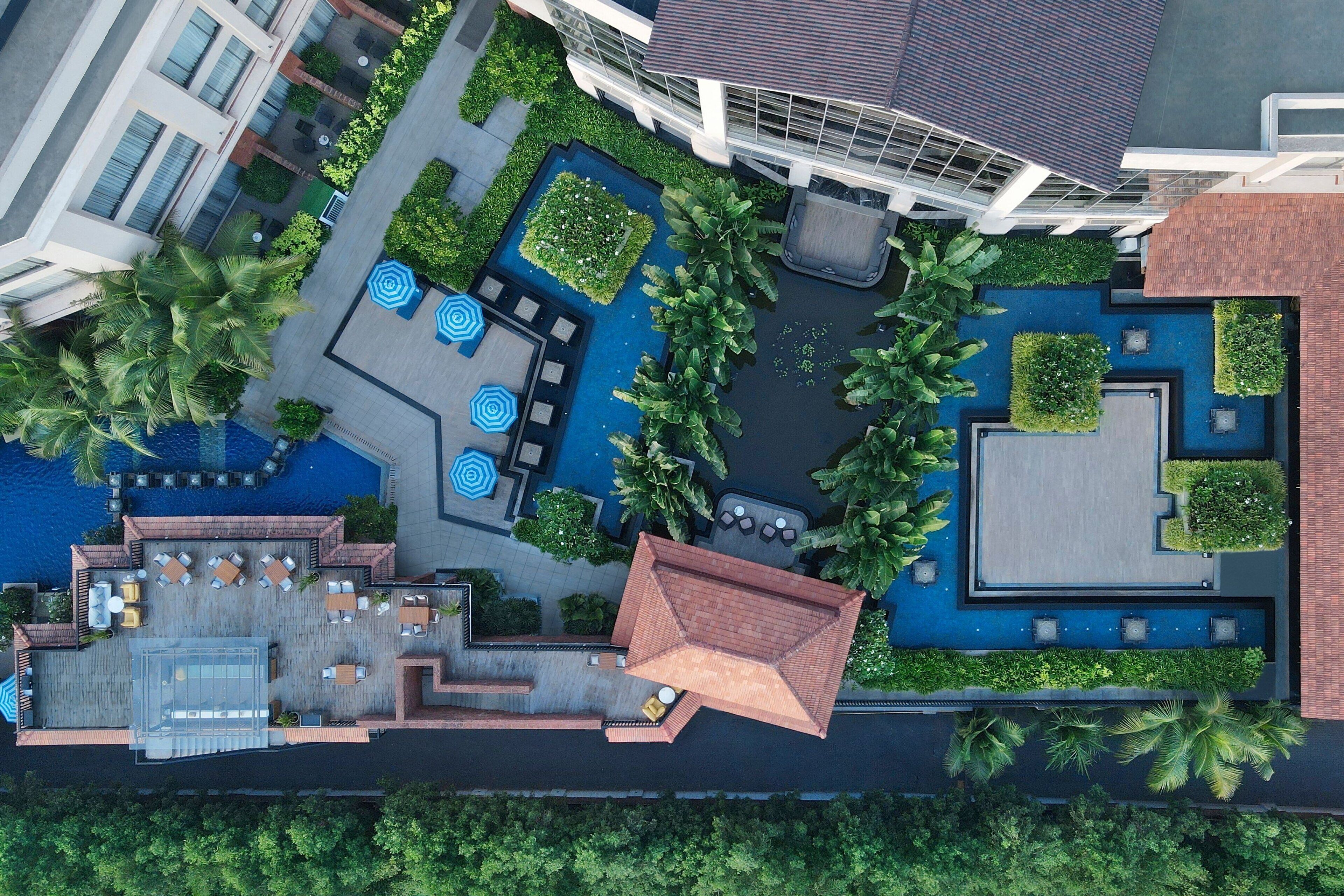 An aerial view of a hotel with a rooftop pool, outdoor seating areas, and lush landscaping.